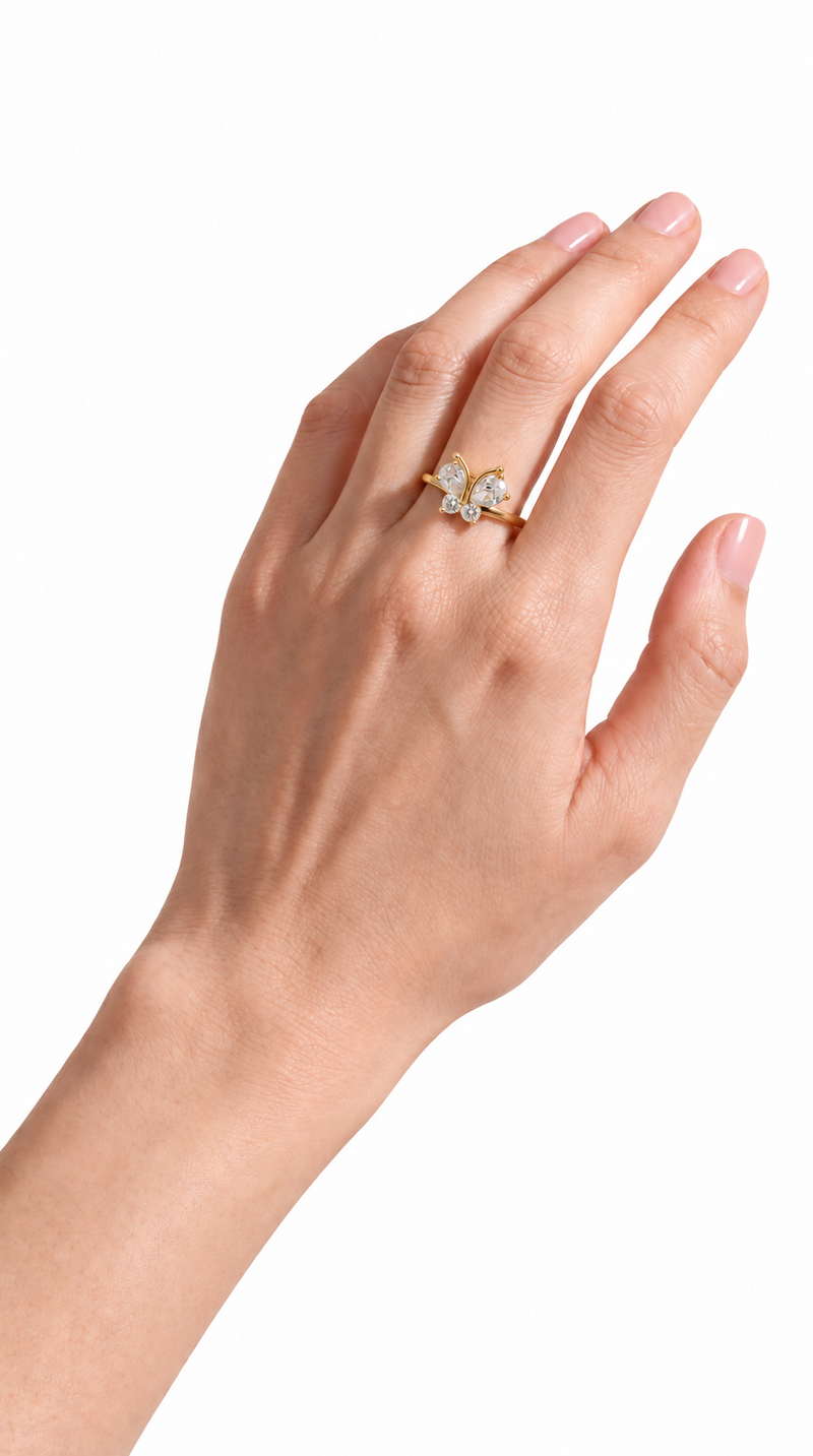 Hand with glossy nude pink nails wearing the Leigh gold butterfly ring against a white background.