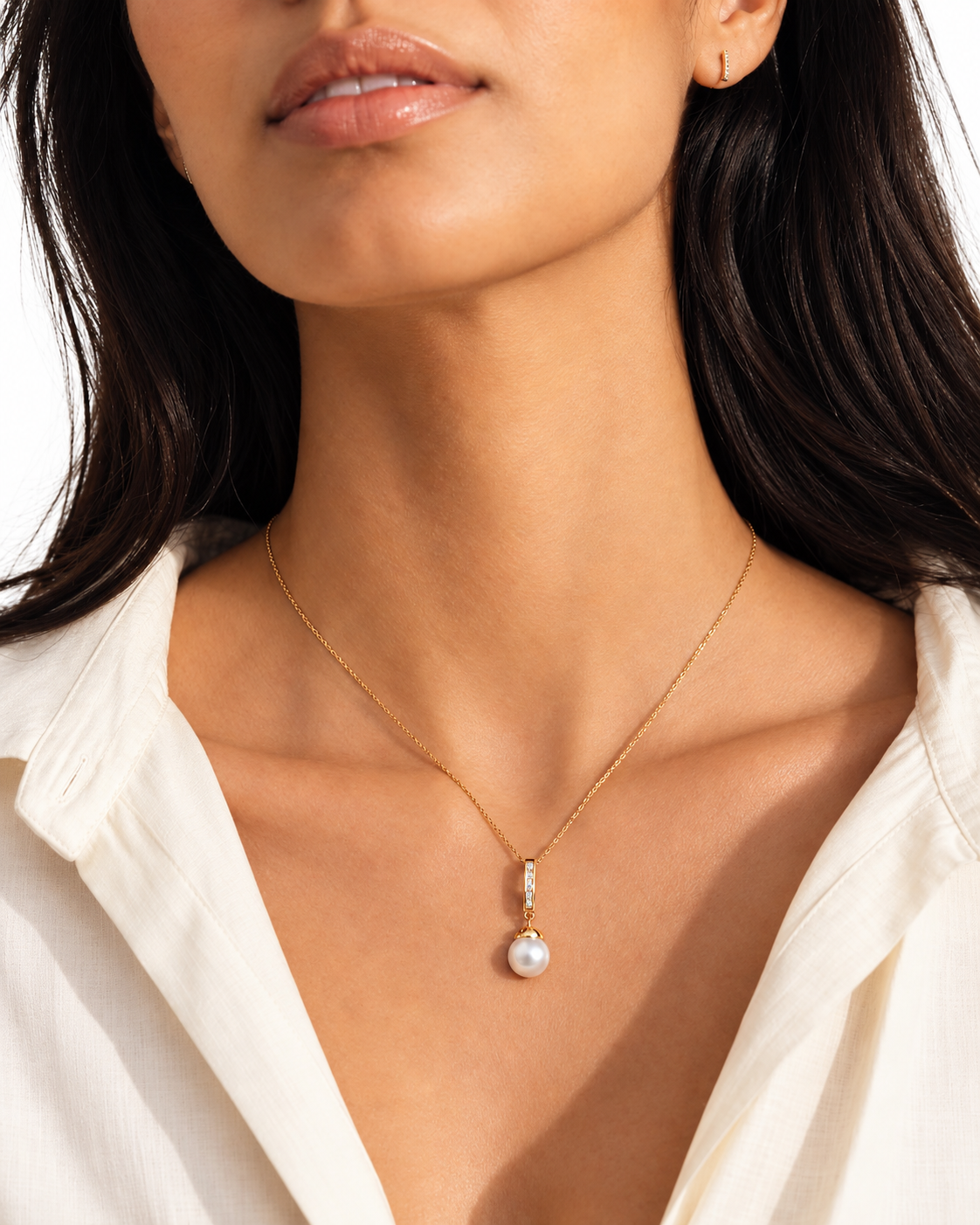 Model wearing the Roma gold necklace with a cubic zirconia bar and white faux pearl drop, styled with a cream shirt against a white background.