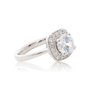 A striking round brilliant cubic zirconia stone surrounded by bead-set cubic zirconia stones evoking a cushion cut guise set in a 925 sterling silver ring. Side view